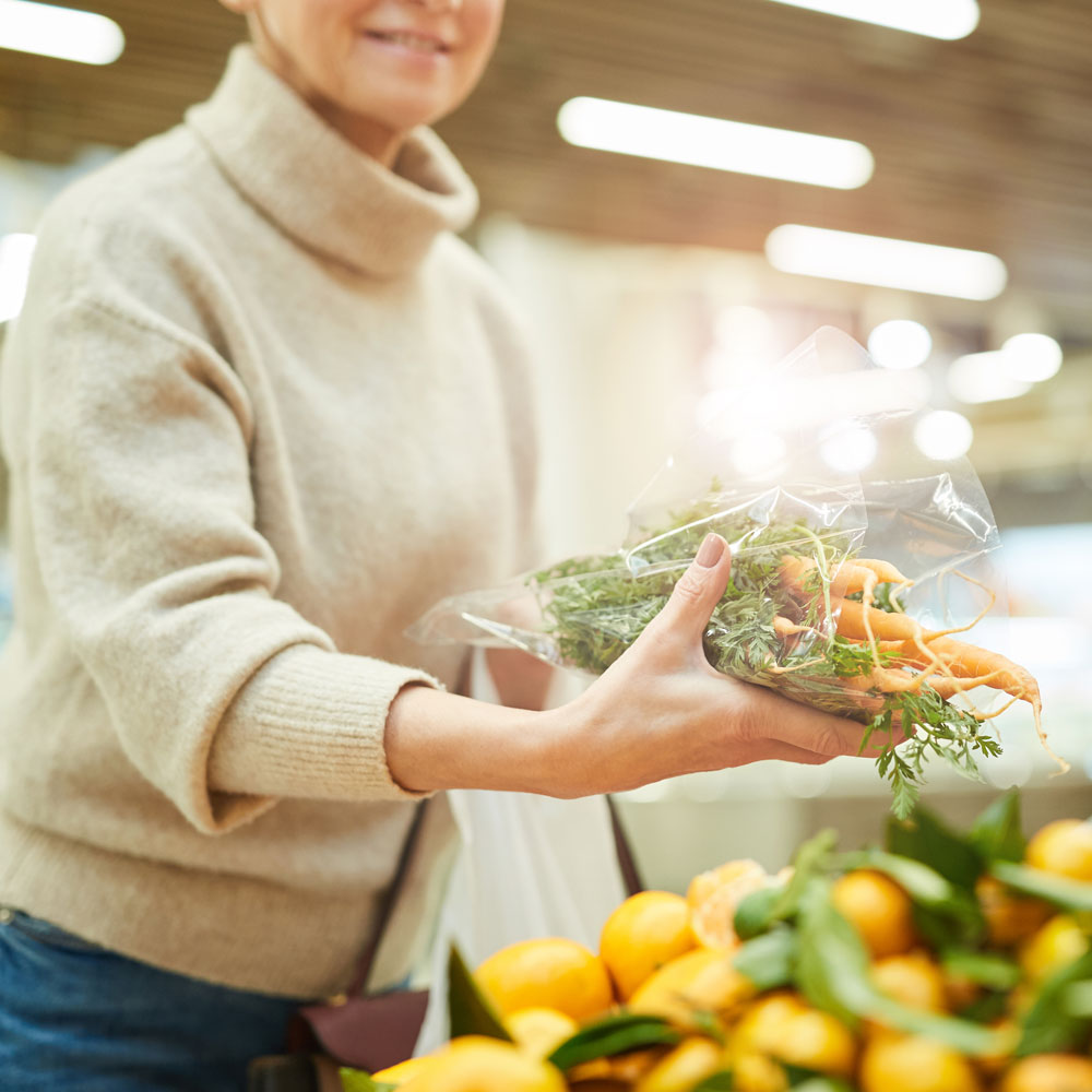 Mujer cogiendo un ramillete de zanahorias en el mercado.