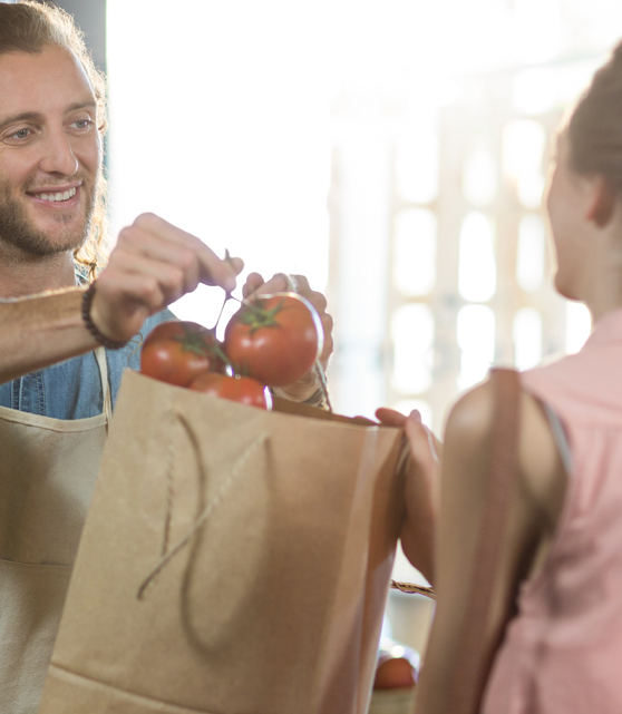 Empleado de mercado entregando unos tomates rama a una clienta