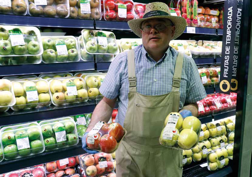 Persona vestida de agricultor sosteniendo dos cajas de manzanas en un supermercado